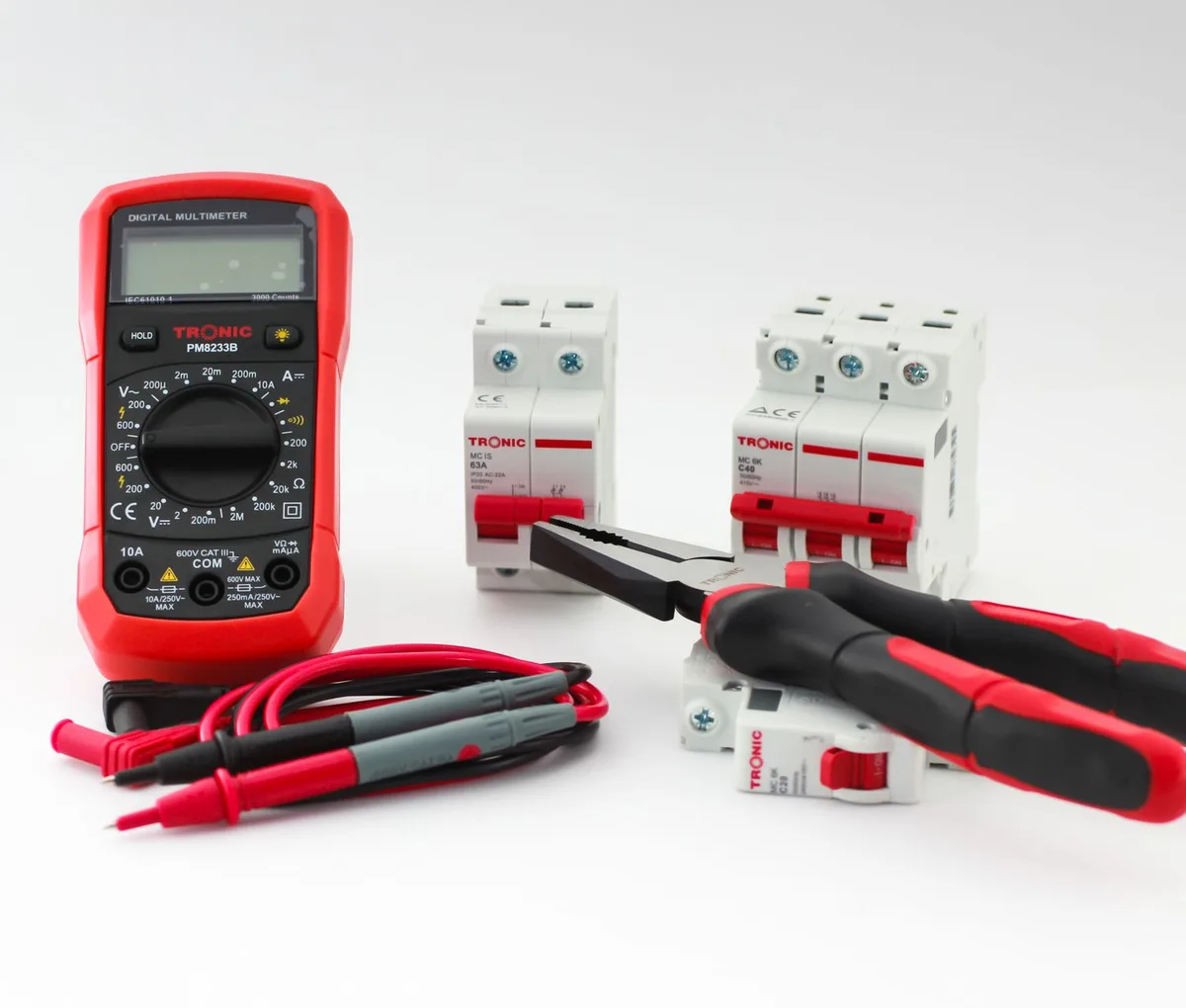 Ein digitales Multimeter, zwei Leitungsschutzschalter, eine Kombizange und ein Schraubendreher liegen auf hellem Untergrund.