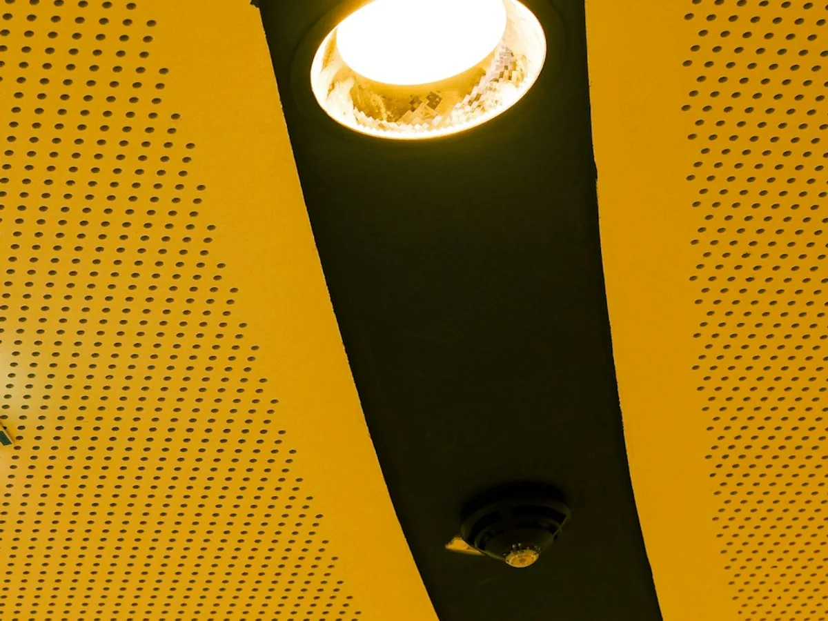 Ein rundes, eingebautes LED-Downlight leuchtet in einem dunklen Deckenkanal zwischen zwei gelben Deckenflächen.